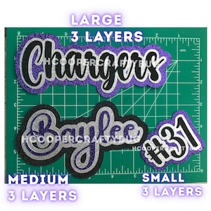 May include: Three layered glitter cardstock cutouts featuring the text Chargers, Baylee, and #31. The designs are arranged on a green cutting mat with inch markings. Each cutout consists of three distinct layers of purple, silver, and black glitter.