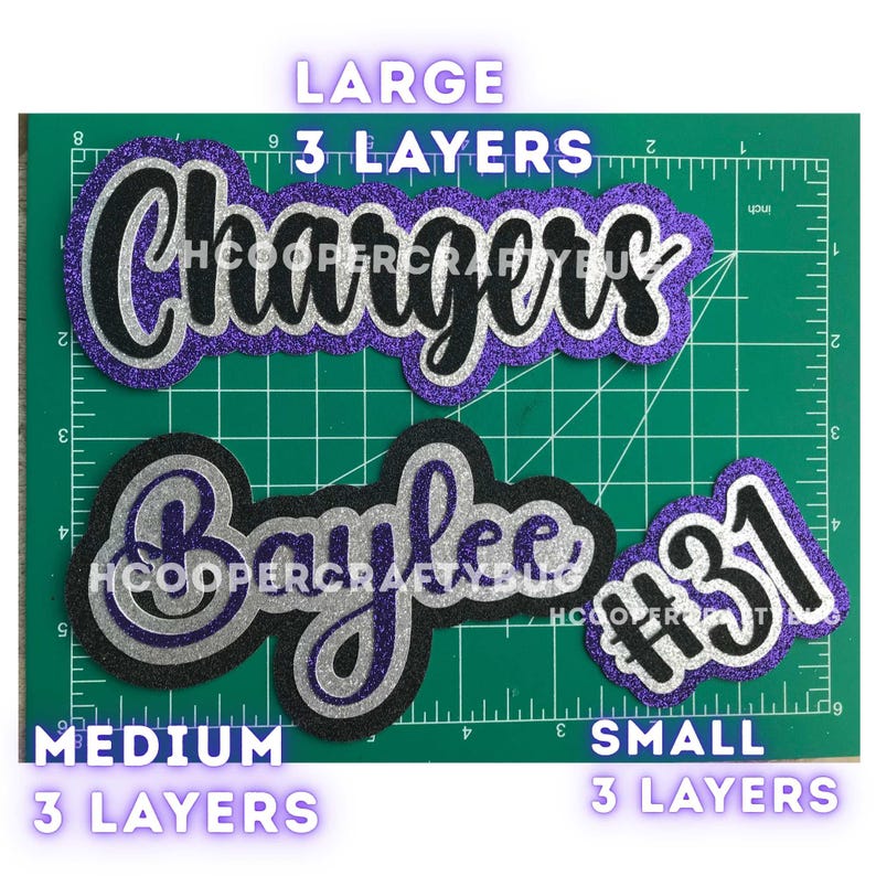 May include: Three layered glitter cardstock cutouts featuring the text Chargers, Baylee, and #31. The designs are arranged on a green cutting mat with inch markings. Each cutout consists of three distinct layers of purple, silver, and black glitter.