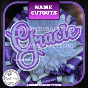 May include: A custom name cutout featuring the name Gracie in a cursive script font. The lettering has a silver glitter finish with a purple glitter outline. It is layered over a white fabric flower and purple and silver glitter ribbon loops.