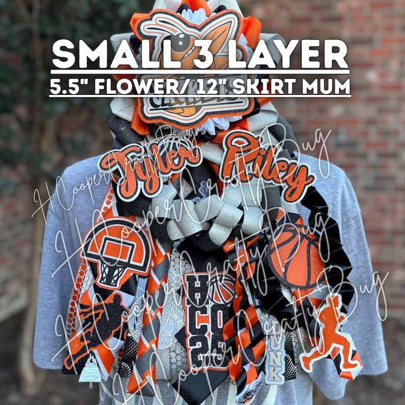 May include: A small 3-layer homecoming mum with a 5.5-inch flower and 12-inch skirt, featuring orange and black ribbons, basketball-themed cutouts, a basketball hoop, and the names Tyler and Riley in glittery orange script on a grey shirt.