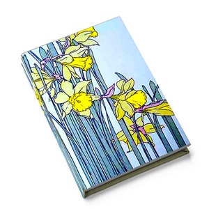 May include: A blue and white notebook with a floral design featuring yellow daffodils. The notebook has a textured cover and a spine.