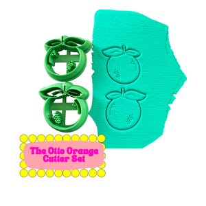 May include: A set of green plastic orange-shaped cookie cutters with leaf and fruit details. Two cutters are shown next to a teal-colored clay sheet with orange imprints. The text "The Otto Orange Cutter Set" is displayed on a pink background.