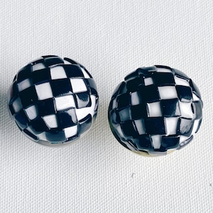 Op de afbeelding: Twee zwart-wit geblokte bolvormige ornamenten. De ornamenten hebben een glanzende afwerking.