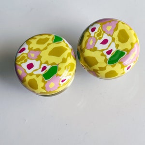 Peut inclure: Deux boutons ronds en céramique à motifs floraux jaunes, roses, verts et blancs.