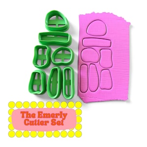 Può includere: Un set di sette tagliapasta in plastica verde con varie forme organiche, accompagnato da un foglio rettangolare di argilla rosa con le relative impronte ritagliate. Un'etichetta riporta il testo The Emerly Cutter Set.