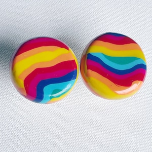 May include: A pair of round, colourful earrings with a rainbow swirl pattern. The earrings are made of a smooth, glossy material and have a bright, cheerful design.