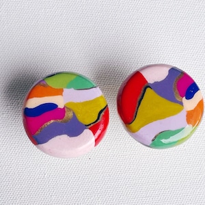 Puede incluir: Un par de pendientes redondos coloridos con patrones abstractos en tonos de rosa, amarillo, verde, azul, rojo y dorado.