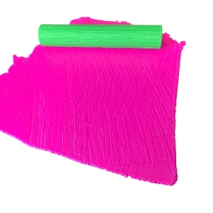 Peut inclure: Un rouleau à pâtisserie vert vif repose sur une feuille d'argile rose vif. L'argile a une surface texturée, et le rouleau est cylindrique avec des rainures visibles. L'image est sur fond blanc, mettant en valeur les couleurs et les textures.