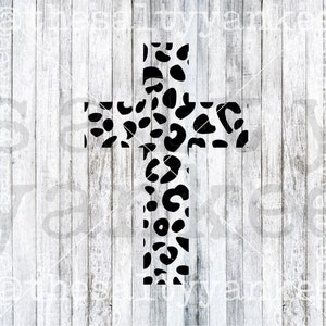 May include: A black and white cross with a leopard print design. The cross is centered on a white wooden plank background. The leopard print pattern consists of black spots on a white background.
