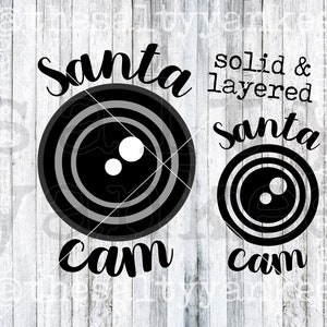 May include: Black and white layered and solid Santa cam SVG design. The design features a stylised camera lens with the words "Santa cam" written below.