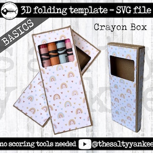 Puede incluir: Un archivo SVG imprimible para una caja de crayones 3D. La caja está decorada con un patrón de arcoíris y corazones. El texto "BASICS" y "Crayon Box" son visibles. El texto "no scoring tools needed" y un botón de reproducción también son visibles. La imagen muestra una caja doblada con crayones adentro y una caja plana desplegada.
