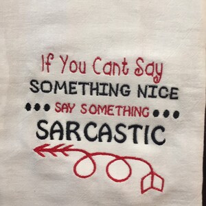 May include: White kitchen towel with red and black embroidery. The text reads "If you can't say something nice... say something sarcastic". A red arrow with a loop is embroidered below the text.