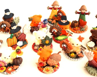 May include: A collection of 12 Thanksgiving themed miniature figurines. The figurines are made of various materials, including plastic, fabric, and metal. They feature a variety of characters, including turkeys, bears, scarecrows, and pumpkins. The figurines are all dressed in festive attire and are perfect for decorating a Thanksgiving table or mantel.