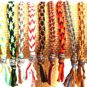 May include: A collection of colorful braided friendship bracelets with tassels and metal beads. The bracelets are displayed on a brown burlap background.