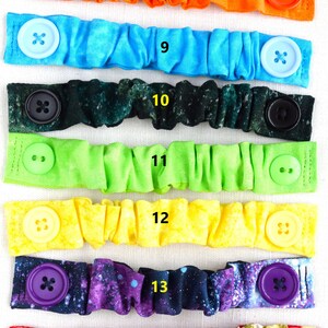 May include: Eight colorful fabric face mask extenders with buttons. The extenders are in a variety of patterns, including orange, blue, green, yellow, and purple. The buttons are also in a variety of colors, including red, blue, black, and purple.