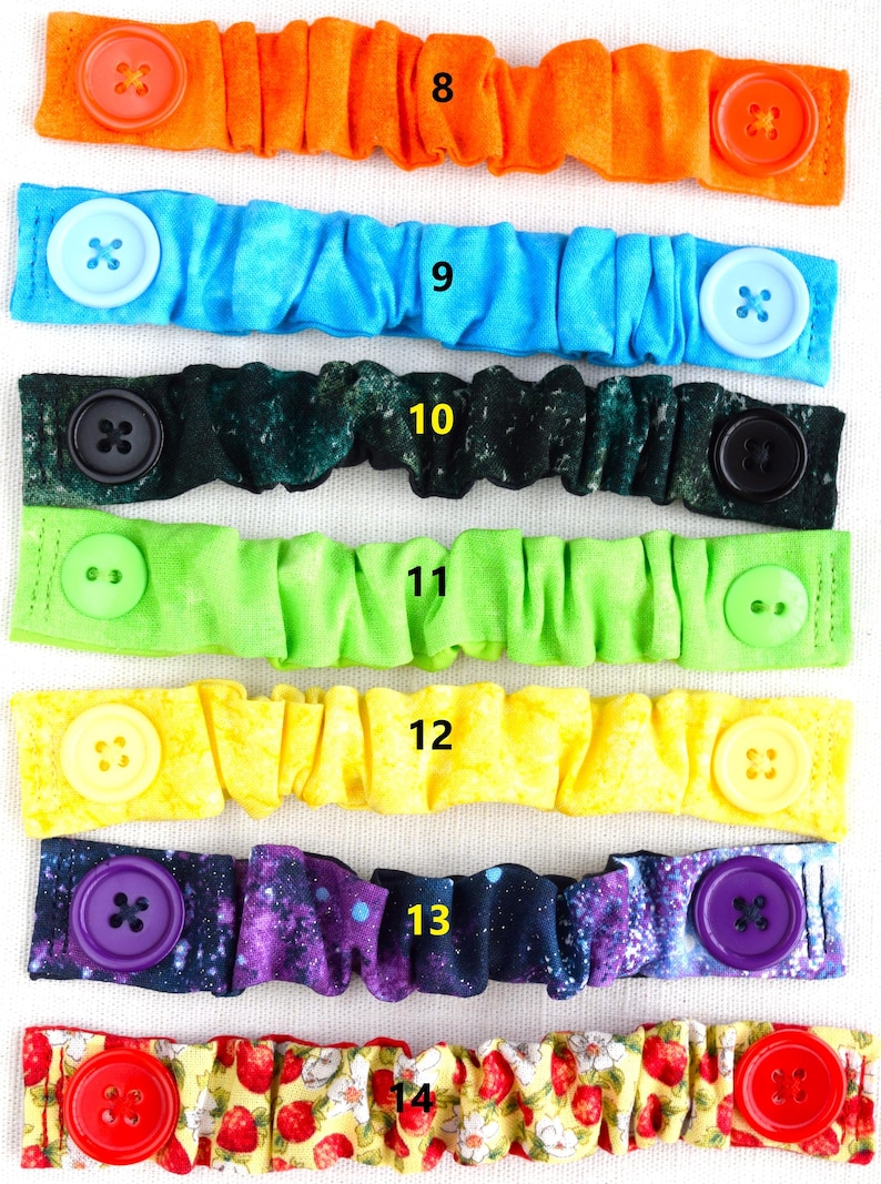 May include: Eight colorful fabric face mask extenders with buttons. The extenders are in a variety of patterns, including orange, blue, green, yellow, and purple. The buttons are also in a variety of colors, including red, blue, black, and purple.