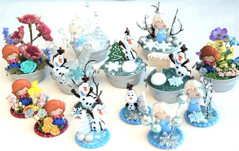 Pu&ograve; includere: Una collezione di scene decorative in miniatura con personaggi di un popolare film d'animazione. Ogni scena &egrave; ambientata in un piccolo secchio di metallo e include statuette, fiori ed elementi a tema invernale. Le scene sono colorate e dettagliate.