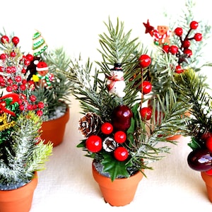 May include: Five small potted Christmas trees decorated with red berries, pine cones, and miniature figurines, including a snowman, a gingerbread person, and a reindeer.