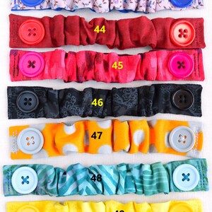 May include: Six colorful fabric face mask extenders with buttons. The extenders are in various patterns, including floral, polka dot, and stripes. The buttons are in various colors, including blue, red, pink, black, gray, and yellow.