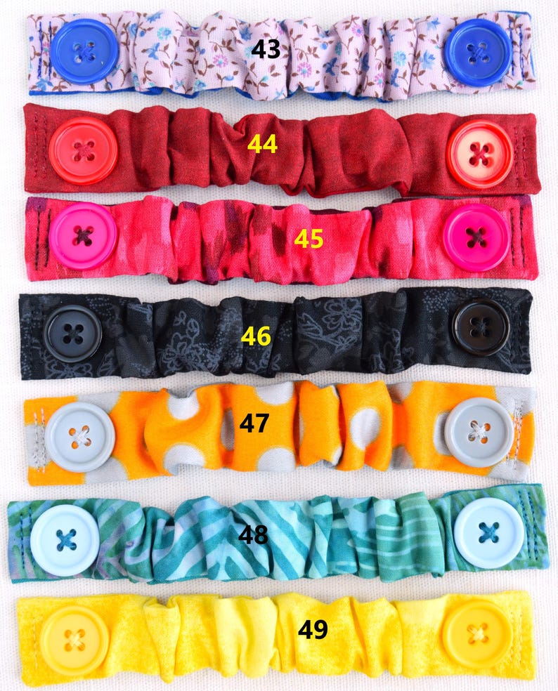 May include: Six colorful fabric face mask extenders with buttons. The extenders are in various patterns, including floral, polka dot, and stripes. The buttons are in various colors, including blue, red, pink, black, gray, and yellow.