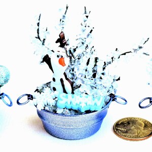 Pu&ograve; includere: Tre composizioni decorative in miniatura a tema Frozen in piccoli secchielli di metallo blu chiaro. Ognuna presenta una statuina di personaggio, neve finta e accenti glitterati. Una moneta &egrave; inclusa per riferimento alle dimensioni.