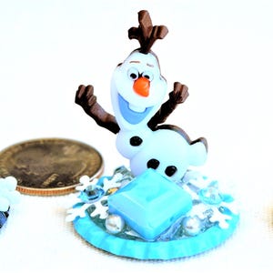Pu&ograve; includere: Tre figurine in miniatura dei personaggi del film d'animazione "Frozen". Le figurine includono Elsa, Olaf e Anna. Ogni figura &egrave; posta su una base con dettagli di fiocchi di neve e gemme. Le figure sono in stile cartone animato.