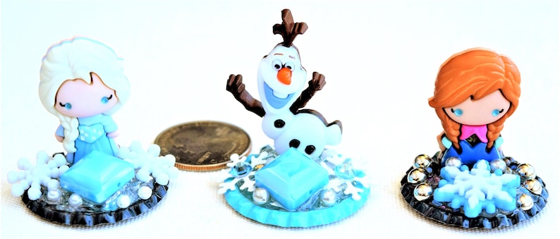 Pu&ograve; includere: Tre figurine in miniatura dei personaggi del film d'animazione "Frozen". Le figurine includono Elsa, Olaf e Anna. Ogni figura &egrave; posta su una base con dettagli di fiocchi di neve e gemme. Le figure sono in stile cartone animato.