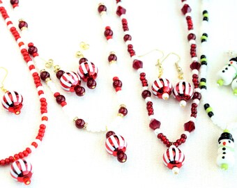 May include: A collection of Christmas-themed jewelry, including necklaces and earrings. The jewelry features red and white striped beads, red beads, and snowman pendants. The earrings have gold-colored hooks.