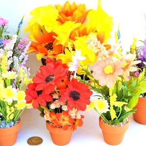 May include: Five potted artificial flower arrangements in terracotta pots. The arrangements feature a variety of flowers in shades of yellow, orange, red, pink, and purple.