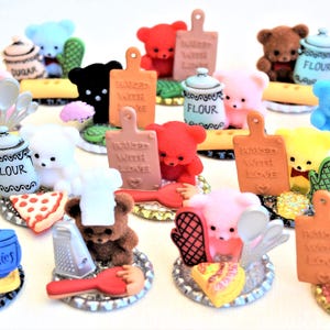 May include: A collection of miniature teddy bear figurines with kitchen-themed accessories. The bears are in various colors, including brown, pink, blue, and yellow. Accessories include cutting boards, jars, and utensils. Some items have text like "Cookies" and "Sugar".