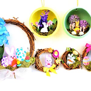 May include: A collection of Easter decorations, including wreaths and hanging baubles. The wreaths are adorned with artificial flowers, eggs, and bunny figurines. The baubles contain miniature scenes with bunnies and flowers.