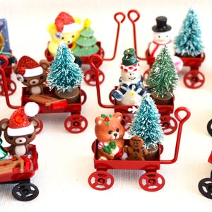 Può includere: Dieci carriole rosse in miniatura con manici in metallo nero, ciascuna riempita con una diversa statuetta in miniatura a tema natalizio e piccoli alberi di Natale artificiali. Le statuine includono un pupazzo di neve, un orso, uno schiaccianoci e un pinguino.