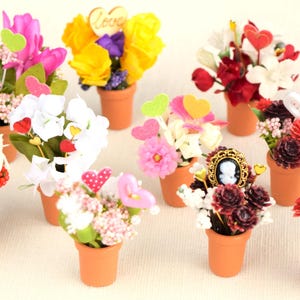 May include: Assortment of miniature potted flowers in various colors, including pink, red, white, purple, and yellow. Each pot is decorated with hearts and the word "Love".