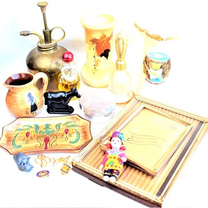 May include: A collection of vintage decorative items, including a brass atomizer, perfume bottles, vases, a small pitcher, a decorative tray, a picture frame, and a doll. The items are in various colors and styles.