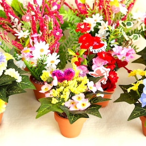 May include: Assortment of small potted artificial flower arrangements in various colors, including yellow, pink, red, blue, and white. The pots are all brown terracotta.