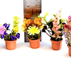 May include: Seven miniature artificial flower arrangements in small terracotta-colored pots. A metal ruler is positioned behind the center pot, showing a height of approximately 1.5 inches for the floral displays, featuring various colors.