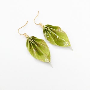 May include: A pair of green origami leaf earrings with gold accents and white floral patterns.