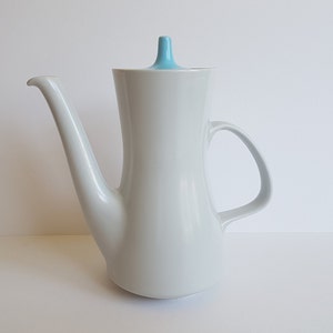 May include: White ceramic coffee pot with a light blue lid. The pot has a curved spout and a handle.