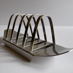 May include: A silver metal toast rack with four slots for holding bread.