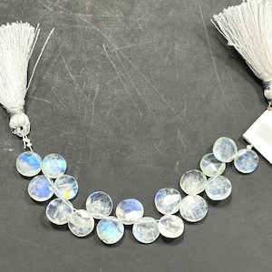 May include: A strand of white moonstone beads with a rainbow iridescent sheen. The beads are round and faceted, and they are strung on a silver wire. The strand is finished with silver tassels on each end.