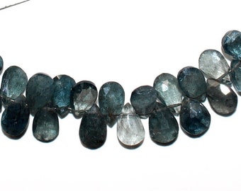 May include: A strand of blue aquamarine gemstone beads with a teardrop shape. The beads are strung on a silver wire and have a white tassel on each end. The strand is approximately 18 inches long.