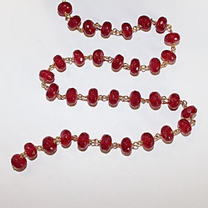 Puede incluir: Una hebra de cuentas de piedras preciosas rojas con eslabones de cadena de oro. Las cuentas son facetadas y tienen una forma ligeramente irregular.