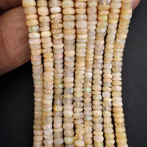 May include: Strands of faceted, light-yellow opal beads. The beads are small, round, and have a subtle iridescence. The beads are strung together, creating a textured and visually appealing surface. The overall effect is delicate and elegant, suitable for jewelry making.