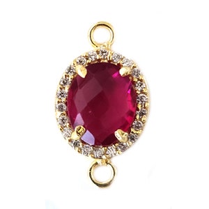 May include: Gold-tone pendant featuring a red gemstone encircled by clear rhinestones. The pendant has two loops for attaching to a chain or cord.