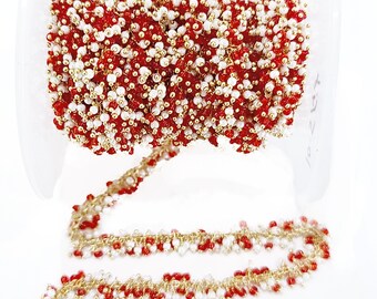 May include: A spool of decorative trim featuring a gold-toned metal chain densely embellished with small, round, faceted red and white beads. The beaded chain is wound around a clear plastic spool, with a length extending downward in a zigzag pattern.
