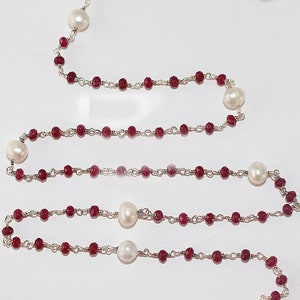 Puede incluir: Un collar largo de cadena de plata con cuentas de piedras preciosas rojas y cuentas de perlas blancas alternadas.