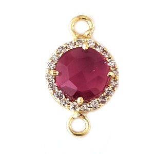May include: Gold-tone connector with a red faceted gemstone surrounded by clear rhinestones. The connector has two loops for attaching jewellery.