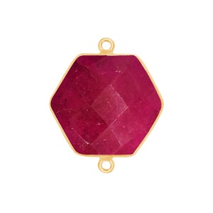 May include: A hexagonal ruby gemstone pendant with gold-toned metal accents. The pendant has two loops for attaching to a chain or cord.
