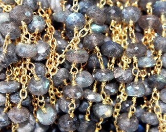 May include: A strand of faceted, round labradorite beads in shades of gray and blue, individually wire-wrapped with gold-toned metal links. The beads exhibit a natural, semi-translucent quality with subtle flashes of iridescent color throughout.