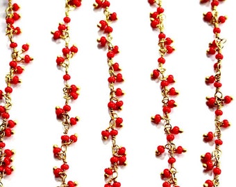 May include: Five vertical strands of gold-toned wire chain adorned with small, round, bright red beads. The beads are attached in clusters along the length of each metallic chain, creating a textured, repetitive pattern of red and gold.